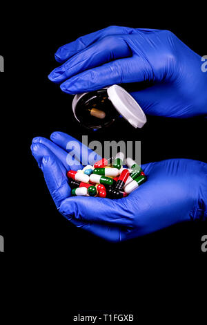 Weibliche Hand, die eine Menge von verschiedenen farbigen Kapseln und Tabletten auf schwarzem Hintergrund isoliert. - Bild Stockfoto