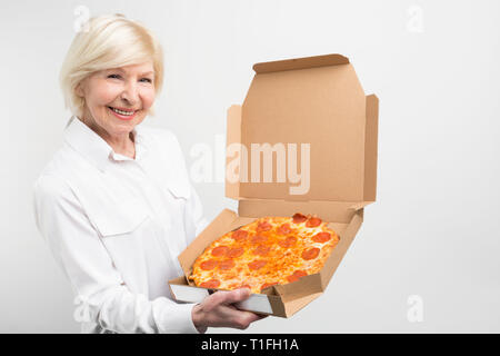 Schnittansicht der Großmutter mit einem grossen Kasten der leckere Pizza. Sie mag die Junk Food despice Es ist nicht gesund für den Menschen. Frau blickt freudig und glücklich Stockfoto
