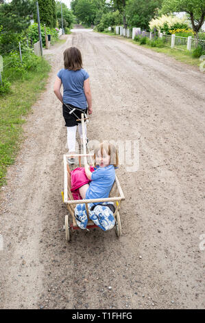 Ältere Mädchen ziehen Jüngere Schwester in einem kleinen Wagen spielen Pferd und Wagen auf der Straße Stockfoto