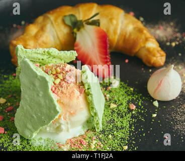 Stück Apfelstrudel mit einer Kugel Vanilleeis auf einer schwarzen Platte, auf einer hölzernen schwarz Tisch, mit Baiser und Erdbeeren dekoriert. close-up Stockfoto