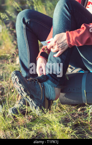 Junge Frau Wanderer mit Rucksack einen Schuh ausziehen eine Putz Hilfe auf ihren Fuß aufgrund der angespannten Schuh im Sommer Urlaub Reise im Wald setzen Stockfoto