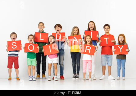 Solidarität mit süßen Herzen. Gruppe von gerne schreiende Kinder, jungen Team oder Jugendliche mit einer roten Fahnen in Weiß studio Hintergrund isoliert. Bildung und Werbung Konzept Stockfoto