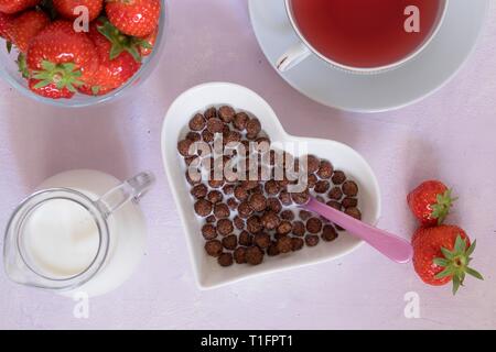 Servieren von Frühstück choco Kugeln Getreide in der Milch. Top down Sicht auf Herzförmige Schale dieser traditionellen Teil des kompletten Frühstück Stockfoto