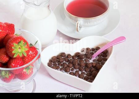 Berühmte Schokolade Getreide als Hauptbestandteil von typischen Frühstück der Kinder. In Herzform Schüssel mit Milch und frischen Erdbeeren serviert. Stockfoto