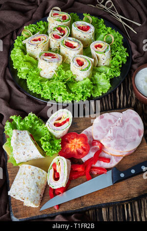 In Scheiben geschnitten sandwich Fladenbrot wraps auf Spieße auf einem Teller. Zutaten und Knoblauch saure Sahne Sauce in einer Schüssel auf einem rustikalen Holztisch mit braunem Stoff, Stockfoto