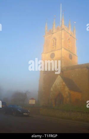 Am frühen Morgen Nebel im Norden Oxfordshire Dorf Hook Norton mit der Pfarrkirche St. Peter emerging Stockfoto