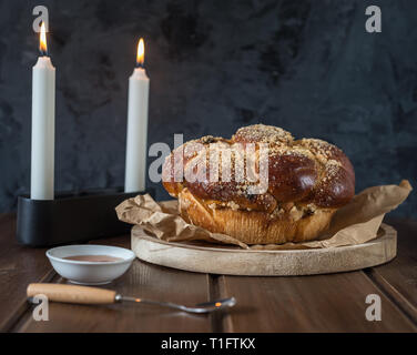 Süße Challah Brot auf einem bewaldeten runde Platte auf Holz braun Tabelle mit Honig und zwei Kerzen am Sabbat Abend machen Kidush/schwarzer Hintergrund mit Stockfoto