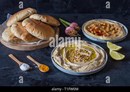 Platten von Hummus mit Fladenbrot auf schwarzem Hintergrund Stockfoto