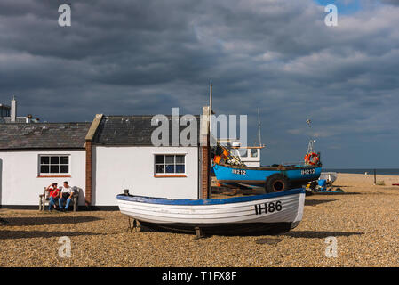 Henne Strand Suffolk UK, mit Blick auf ein Paar mittleren Alters entspannen neben Fischerbooten am Strand von Aldeburgh, Suffolk, England, UK. Stockfoto