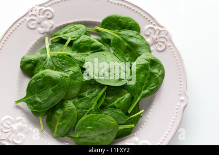 Junge Blätter Spinat auf einem Teller. Ansicht von oben, weißer Hintergrund, kopieren. Detox, eine diätetische Lebensmittel Zutat - grün Bio Spinat Stockfoto