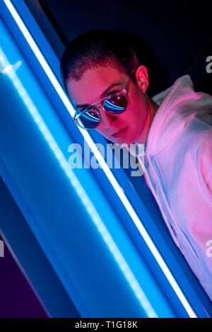 Bunte Porträt einer jungen Frau mit kurzen Haaren glänzende Sonnenbrille und Stellung im Neonlicht. Stockfoto