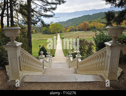 Ein weißer Stein Treppe im Herbst Garten führt an die gelbe Bäume im Herbst auf einem Hintergrund der Berge mit Herbst Wolken