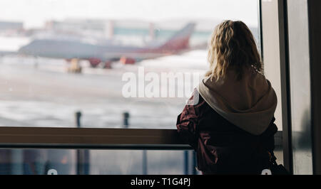 Foto von der Rückseite der Blonde in der Nähe der Fenster mit dem Flugzeug fliegen am Nachmittag. Stockfoto