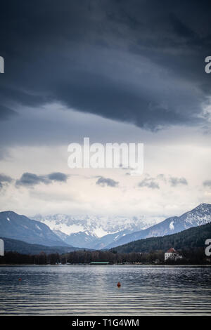 Blick vom See Wörthersee zu Bergkette Koschuta an einem bewölkten Frühling in Kärnten, Österreich Stockfoto