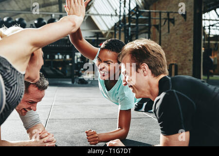 Zwei Lachende junge Frauen in Sportbekleidung hohe fiving einander beim Beplankung mit ein paar männliche Freunde auf einen Fitnessraum, Stockfoto