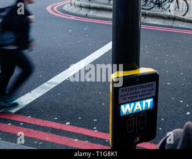 Ein fussgänger ist die Straße überqueren, obwohl 'Warten' Zeichen Warnleuchte an der Fußgängerzone Schaltkasten leuchtet. Stockfoto