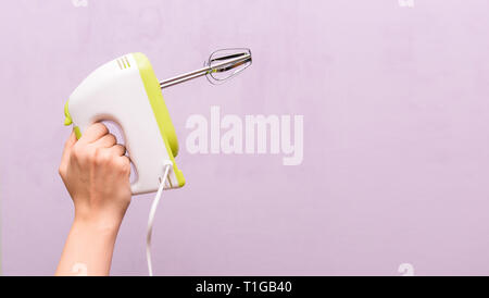 Weibliche Hand ein Mischpult. Küche elektrisches Gerät auf einem violetten Hintergrund. Frau Hausfrau Stockfoto