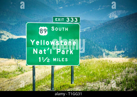 Eine grüne Montana Autobahnausfahrt Zeichen für Yellowstone National Park, mit Bergkulisse auf der I-90 Autobahn Stockfoto