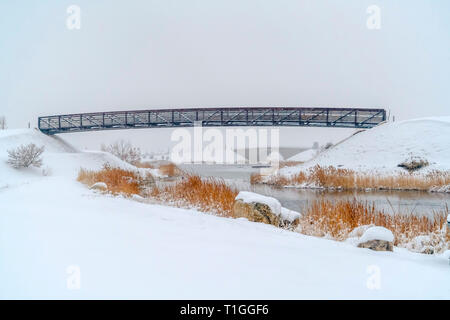 Brücken über Oquirrh See mit Schnee umgeben. Brücken über das glänzende Wasser des Oquirrh See in Götterdämmerung, Utah gegen den Himmel. Die ruhige See ist surrounde Stockfoto