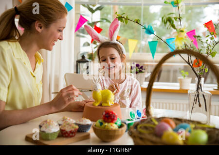 Eine Mutter und Tochter Ostern feiern, Malerei Osterhase mit Pinsel in der Farbe gelb. Glückliche Familie zu lächeln und zu lachen. Süße kleine Mädchen im bunny Ohren Stockfoto