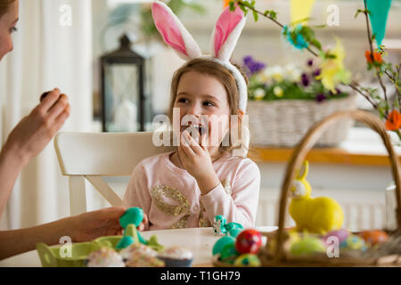 Mutter und Tochter Ostern feiern, Schokolade essen Eier. Happy Family Urlaub. Süße kleine Mädchen mit lustigen Gesicht in Hasenohren lachen, lächeln Stockfoto