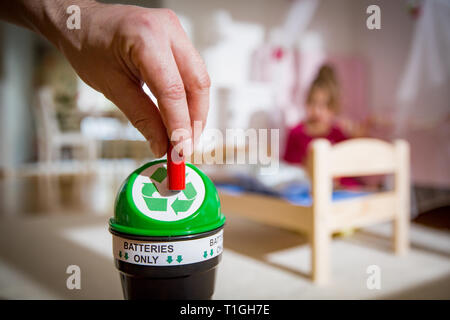 Mann, gebrauchte Batterien in Recycling Box zu Hause. Kind im Kinderzimmer mit Spielzeug spielen. Trennung von Abfällen Konzept. Batterien nur. Stockfoto