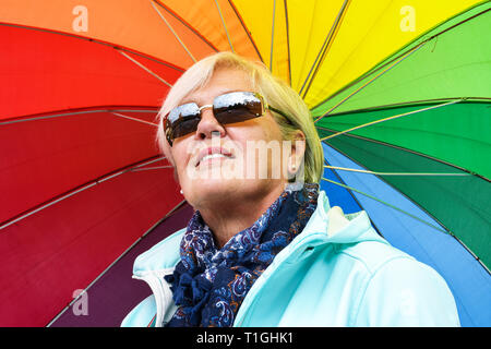 Im mittleren Alter grau behaarte Frau bunten Regenschirm außerhalb Holding an einem sonnigen Tag im Herbst Stockfoto