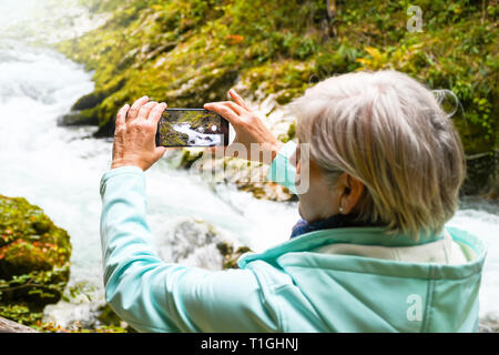 Schöne attraktive ältere, reife Frau mit glänzenden grauen Haaren fotografieren und selfies Outdoor in einer Schlucht Vintgar River Canyon Schlucht an einem sonnigen Tag Stockfoto