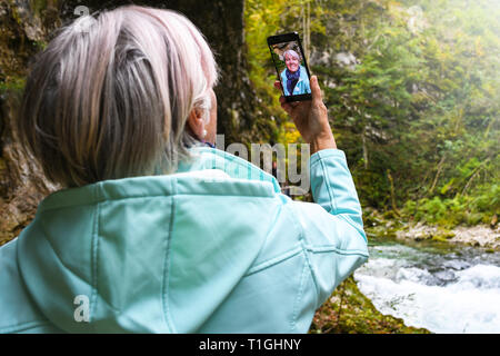 Schöne attraktive ältere, reife Frau mit glänzenden grauen Haaren fotografieren und selfies Outdoor in einer Schlucht Vintgar River Canyon Schlucht an einem sonnigen Tag Stockfoto