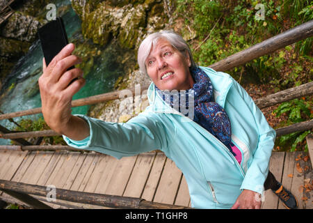 Schöne attraktive ältere, reife Frau mit glänzenden grauen Haaren fotografieren und selfies Outdoor in einer Schlucht Vintgar River Canyon Schlucht an einem sonnigen Tag Stockfoto