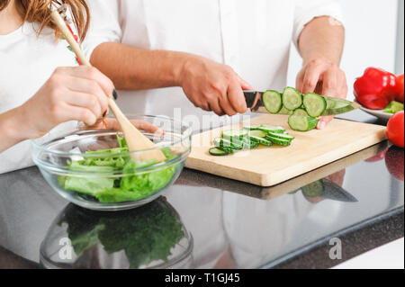 Familie zusammen kochen Mann schneiden grüne Gurke und Frau blending Salatblätter Stockfoto