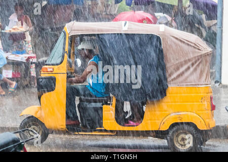 Nosy Be Madagaskar - 17 Januar 2019: ein Mann, der ein Tuk-Tuk unter starker Regen in Nosy Be Madagaskar. Stockfoto