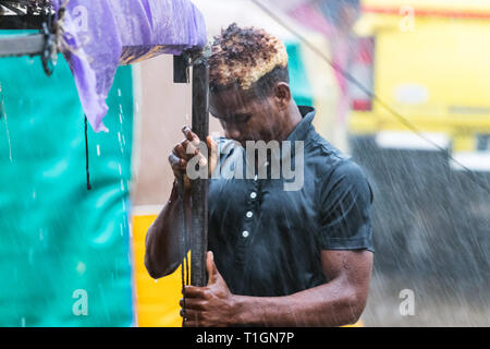 Nosy Be Madagaskar - 17 Januar 2019: ein Mann bei der Arbeit neben der Straße unter einem schweren Regen in Nosy Hinhaltestrategie, Madagaskar. Stockfoto