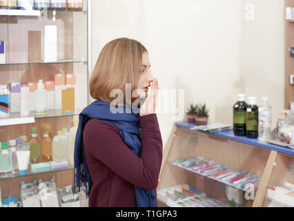 Kranke Frau, die in der Apotheke, Husten, der den Mund mit der Hand. Weibliche Kunden, Medikamente und Pillen von der Krankheit. Kranke Frau mit kurzen kastanienbraune Haare mit blauen Schal. Stockfoto