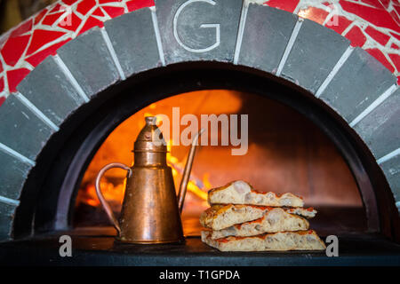 Scheiben der traditionellen römischen Stil Pizza im Mund der Holzofen in einer Trattoria, Pizzeria mit Messing Olivenöl Flasche Backofen Stockfoto