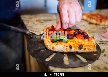 Ein Koch Mann legt den letzten Schliff in römischem Stil italienische Pizza in einer Trattoria/Pizzeria. Vorbereitung Pizza. Selektiver Fokus Stockfoto