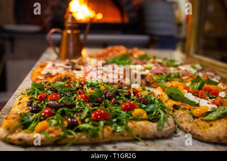 Bunte authentisch römischen Stil italienische Holzofen Pizza auf Zähler vor dem Holzfeuer Ofen. In einer Trattoria/Pizzeria/Restaurant Stockfoto