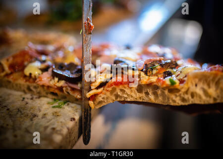 Ein Stück der traditionellen römischen Stil Holzofen Pizza mit einem Messer in einer italienischen Pizzeria/Trattoria/Restaurant abgeschnitten zu sein. Selektiver Fokus Stockfoto