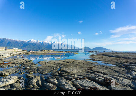 Die schneebedeckten Kaikoura Berge in Ruhe rockpool auf Schlamm wider - Stein Felsvorsprung Stockfoto