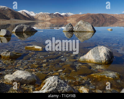 Blaues Wasser und braun Pisten mit Schnee auf Dächern von pangong See, im Vordergrund riesigen Steinen, Indien. Stockfoto