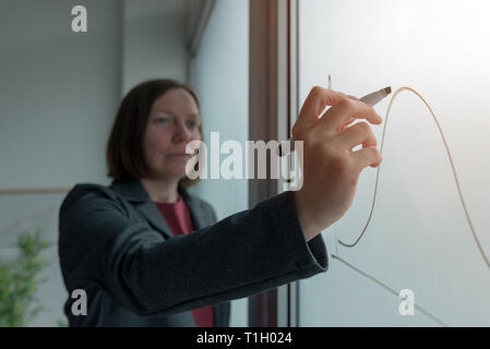 Geschäftsfrau Zeichnung Grafik auf dem Whiteboard im Büro während der Präsentation der Ergebnisse beim Corporate Meeting Stockfoto