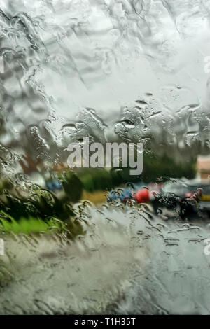 Regen auf dem nassen Auto Windschutzscheibe mit Unscharf suburban Wohnstraße im Hintergrund. Stockfoto