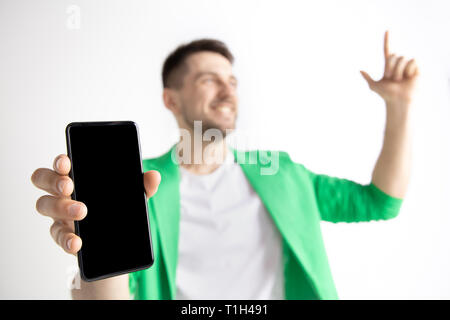 Sein kühles. Gute Nachrichten. Tun, wie mich. Jungen gutaussehenden Mann zeigt der Bildschirm des Smartphones und Unterzeichnung OK Zeichen auf grauem Hintergrund. Menschliche Emotionen, Fa Stockfoto