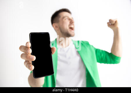 Sein kühles. Gute Nachrichten. Tun, wie mich. Jungen gutaussehenden Mann zeigt der Bildschirm des Smartphones und Unterzeichnung OK Zeichen auf grauem Hintergrund. Menschliche Emotionen, Fa Stockfoto