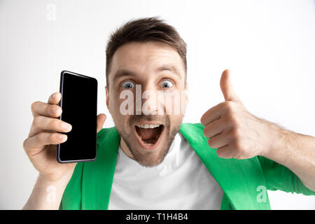 Sein kühles. Gute Nachrichten. Tun, wie mich. Jungen gutaussehenden Mann zeigt der Bildschirm des Smartphones und Unterzeichnung OK Zeichen auf grauem Hintergrund. Menschliche Emotionen, Fa Stockfoto