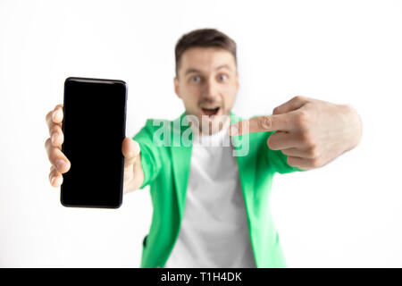 Sein kühles. Gute Nachrichten. Tun, wie mich. Jungen gutaussehenden Mann zeigt der Bildschirm des Smartphones und Unterzeichnung OK Zeichen auf grauem Hintergrund. Menschliche Emotionen, Fa Stockfoto