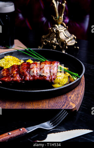 Schließen Sie herauf Gourmet Hauptspeise mit gegrilltem Schweinefleisch Rippe und Bratkartoffeln auf Schwarz pan. Auf Holzbrett serviert. Stockfoto