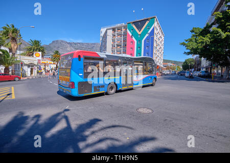 Myciti bus Wenden auf der Straße in der Mitte mit dem Tafelberg im Hintergrund, und Apartment Gebäude in Farbe der Flagge. Kapstadt, Südafrika, Stockfoto
