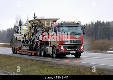 Mariehamn, Finnland - 23. März 2019: Rot Volvo FH 520 Auflieger von Konekuormaus Seppanen Oy hols Metso Lokotrack LT1110 Schlagkörper Anlage entlang der Autobahn. Stockfoto