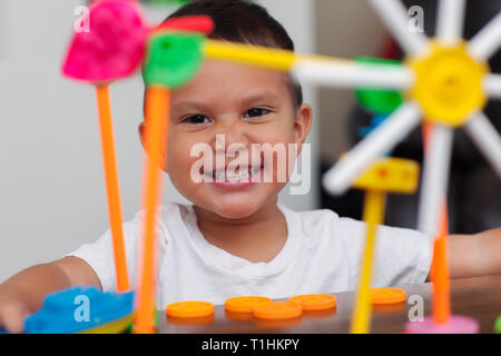 Ein Hispanic junge mit großen Lächeln, während er mit bunten Gebäude Spielzeug spielt und lernt, sich mit elementaren manipulative Spielzeug zu zählen. Stockfoto